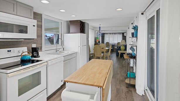 Une cuisine moderne avec des appareils électroménagers blancs, une table à manger en bois et une vue sur l’espace de vie.