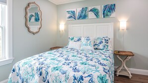 Quarto com cama, mesa de cabeceira, espelho fixado na parede e obras de arte nas paredes.