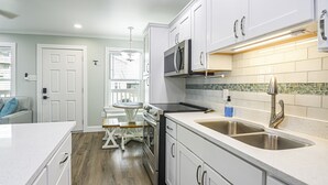 Cozinha moderna com armários brancos, eletrodomésticos de aço inoxidável, uma pia dupla e um espaço de jantar com mesa e cadeiras.