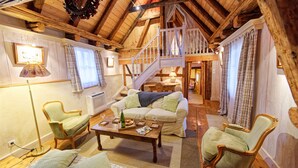 A cozy room with a wooden ceiling, a staircase, a sofa, a table with glasses, and a chair. - The Doves' nest House in the rempart (Riquewihr)