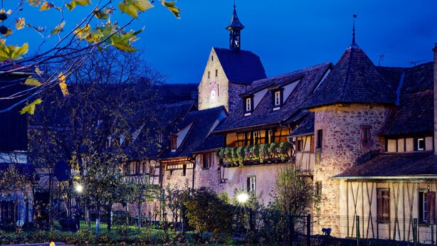 A traditional European village with stone buildings, a prominent church tower, and a well-maintained garden. - The Doves' nest House in the rempart (Riquewihr)