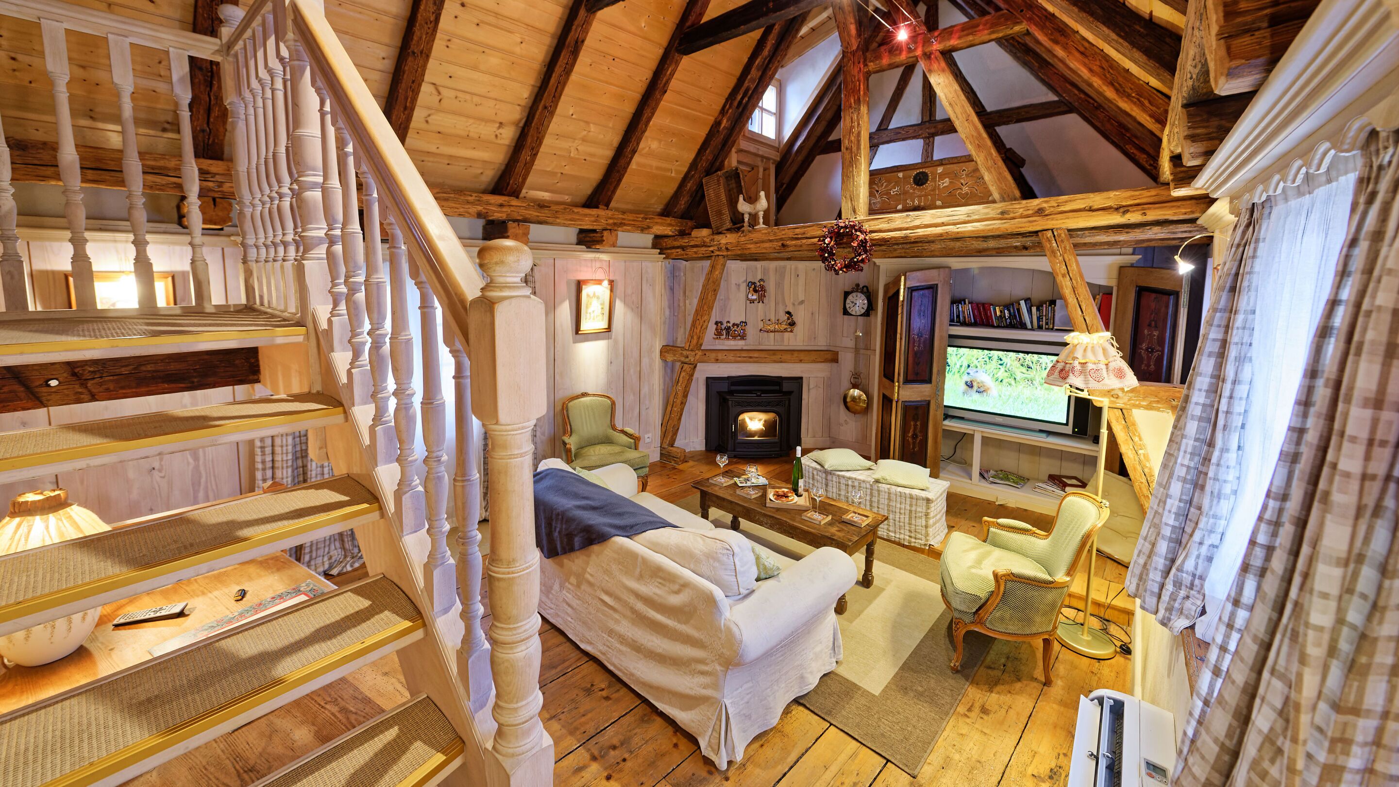 Un salon chaleureux de style loft, doté d’une cheminée, d’un escalier en bois et d’un téléviseur.