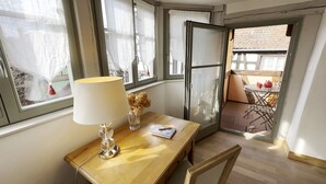 Una habitación con un escritorio de madera, una lámpara, un jarrón con flores secas y vistas a un patio exterior con una mesa y sillas.