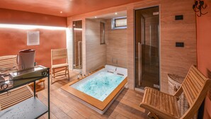 Une salle de spa équipée d’un bain à remous, de chaises en bois, d’une table en verre et d’un espace douche.