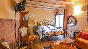Une chambre d’hôtel avec un lit, une chaise, une petite table, un canapé, un miroir et une fenêtre.