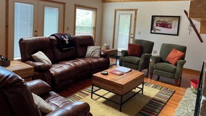 A cozy living room with a brown leather couch, a green armchair, and a wooden coffee table. There are two windows with blinds, a door, and a framed picture on the wall. - Mountain Villa with amazing views, Hot tub, and game room, (Marble)