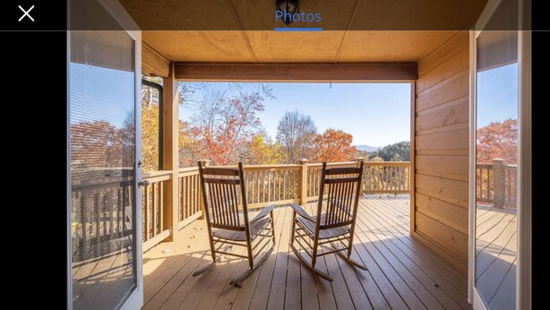 A wooden deck with two rocking chairs and a table, overlooking a scenic view with autumn foliage. - Mountain Villa with amazing views, Hot tub, and game room, (Marble)