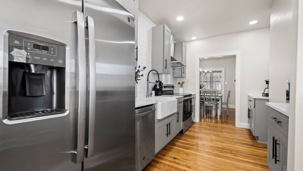 A modern kitchen with stainless steel appliances, grey cabinets, and a wooden floor.