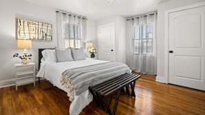 A bedroom with a large bed, bedside tables, a bench, and a chandelier.