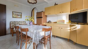 A dining area with a table and chairs, a vase with sunflowers, and wooden cabinets. - 981 Villa Delle Rose - Appartamento A (Porto Cesareo)
