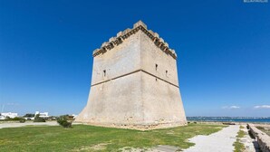 A historic stone tower with a flat top and a base surrounded by a grassy area. - 981 Villa Delle Rose - Appartamento A (Porto Cesareo)