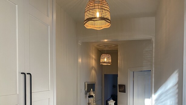 A hallway with white walls, a wooden floor, and a white railing. There are two hanging lights and a door at the end. - Stylish Apt London Excel Olympic Close to Station (London)