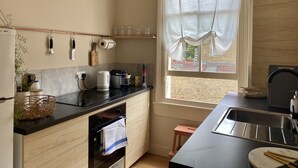 A modern kitchen with a black countertop, wooden cabinets, a built-in oven, and a window with curtains. - Stylish Apt London Excel Olympic Close to Station (London)