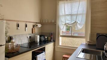 A modern kitchen with a black countertop, wooden cabinets, a built-in oven, and a window with curtains.