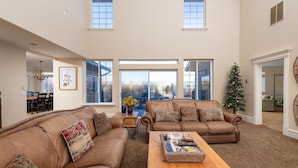 A spacious living room with two brown leather sofas, a wooden coffee table, and a large window offering a view of the outdoors. - Family Getaway~hot Tub, Ice Castles & Tubing Hs 5 Bedroom Home by RedAwning (Midway)