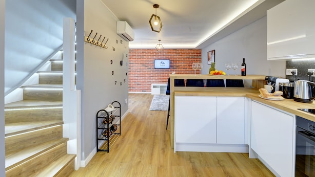 A modern kitchen with a central island, wooden flooring, and a brick wall in the background. - Modern 2BR House & Private Parking & Kid-friendly (Rugby)