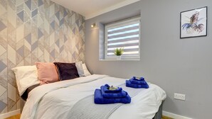 A neatly made bed with a geometric patterned wall, a small window with blinds, and a power outlet on the wall. - Modern 2BR House & Private Parking & Kid-friendly (Rugby)