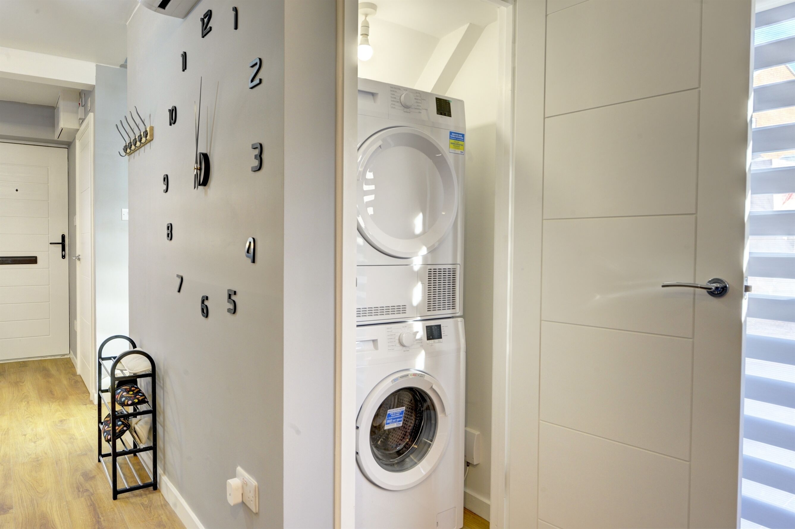 Une buanderie avec une horloge murale, un lave-linge blanc et un étendoir sur lequel sont pliés des vêtements.