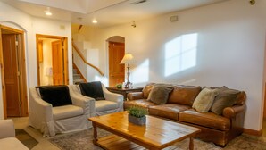 A living room with a brown leather sofa, white armchairs, a wooden coffee table, and a patterned rug. - Family Vacation~heated In/out Pool, Tubing & Ice Skating 719 3 Bedroom Townhouse by RedAwning (Midway)