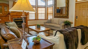 A living room with a leather sofa, a wooden coffee table, a lamp, and a fireplace. - Family Vacation~heated In/out Pool, Tubing & Ice Skating 719 3 Bedroom Townhouse by RedAwning (Midway)