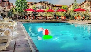 A swimming pool with lounge chairs and umbrellas, surrounded by buildings. - Family Vacation~heated In/out Pool, Tubing & Ice Skating 719 3 Bedroom Townhouse by RedAwning (Midway)