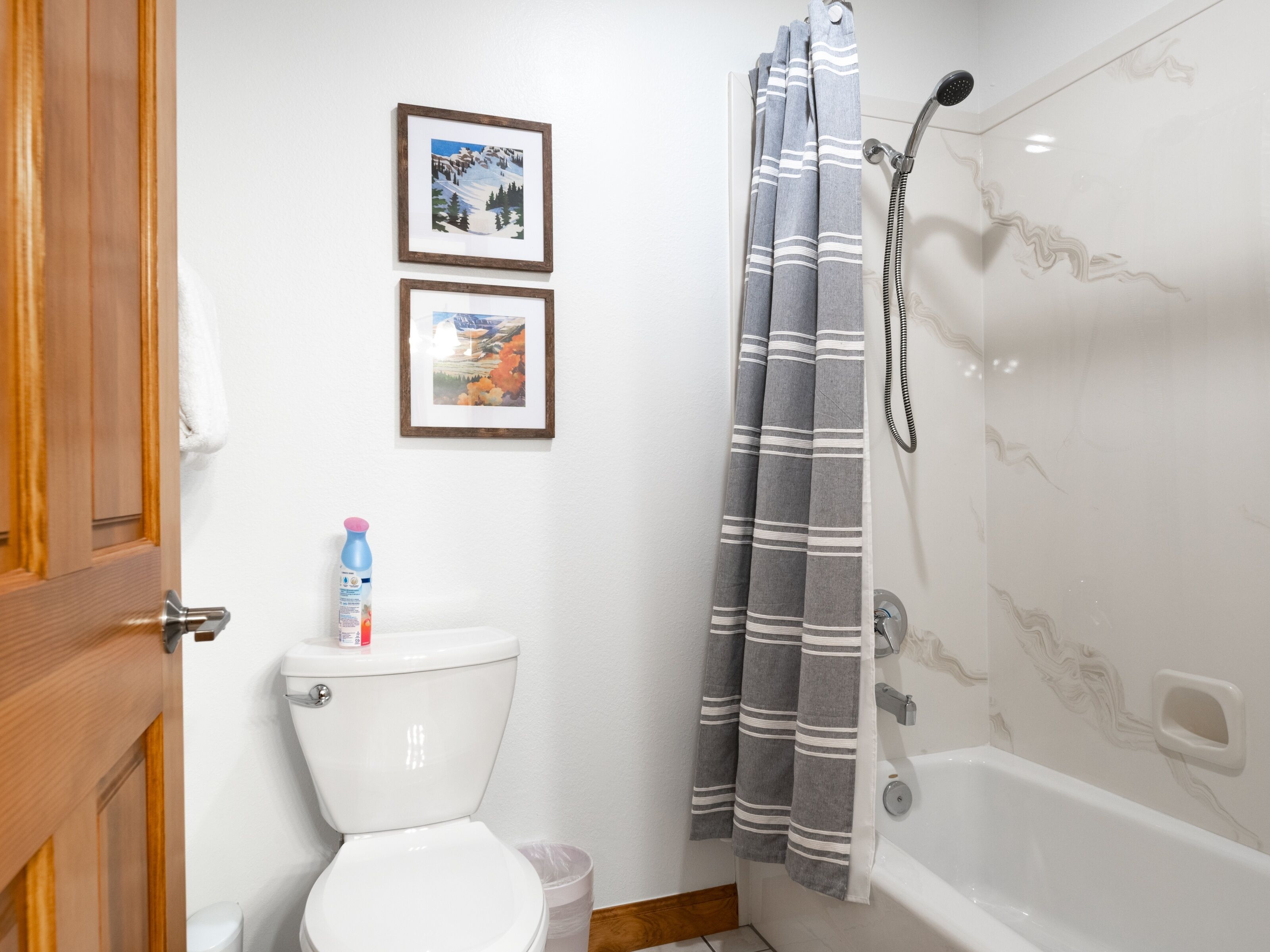 A bathroom with a toilet, a shower with a striped curtain, and two framed pictures on the wall.