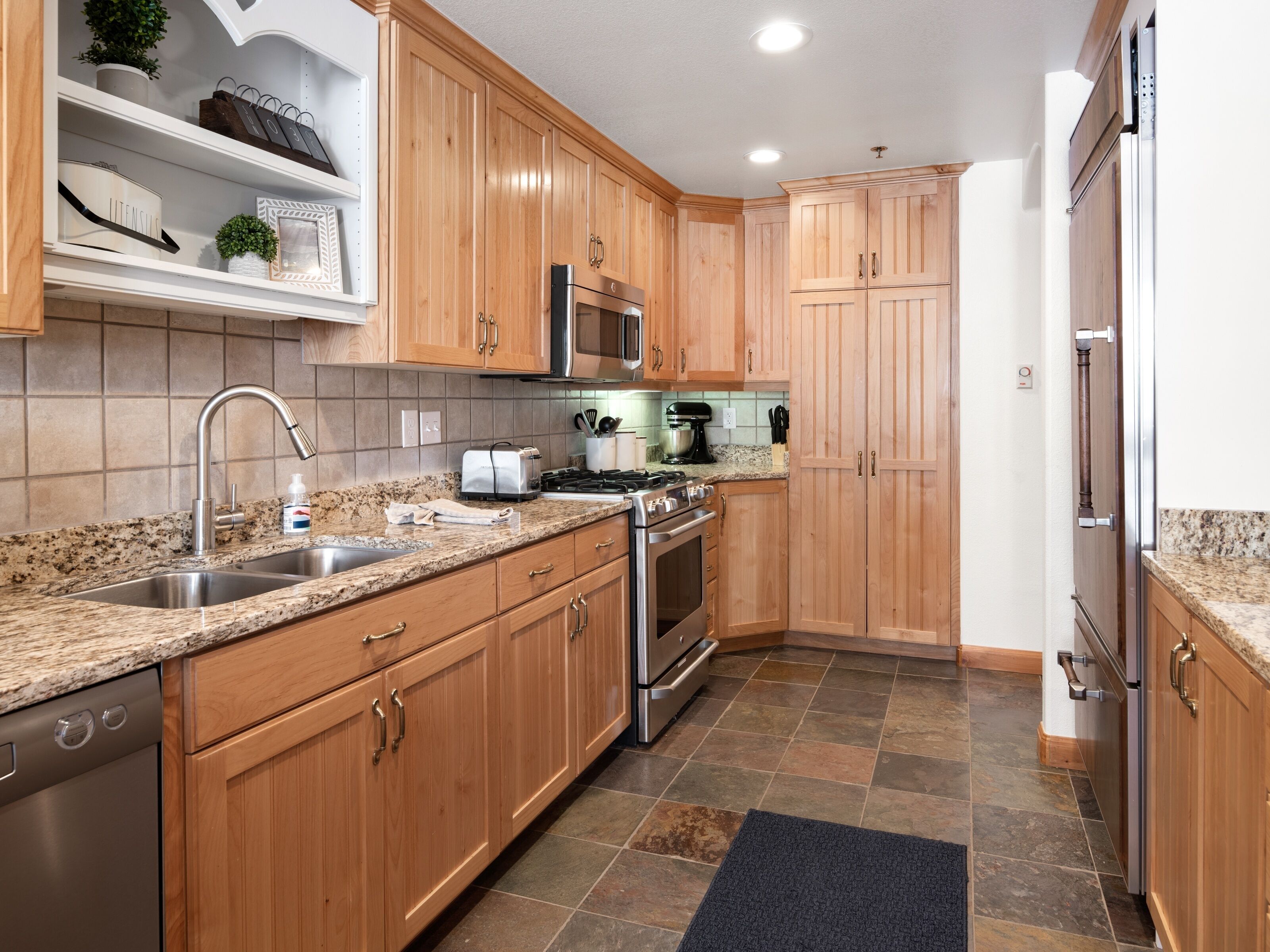 A modern kitchen with wooden cabinets, stainless steel appliances, granite countertops, and a tiled backsplash.