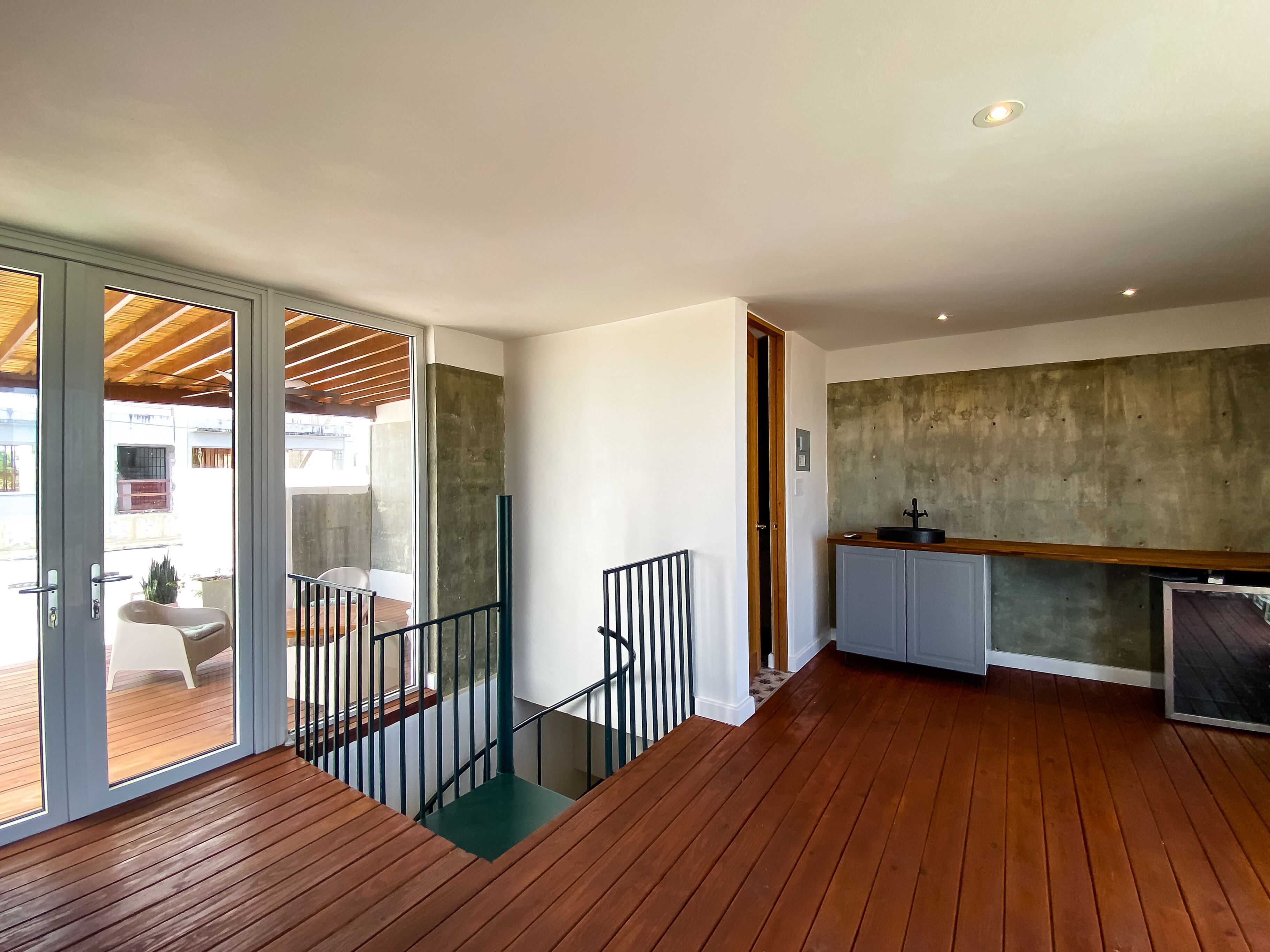 A modern interior with a wooden staircase, a kitchen area, and a balcony with outdoor furniture.