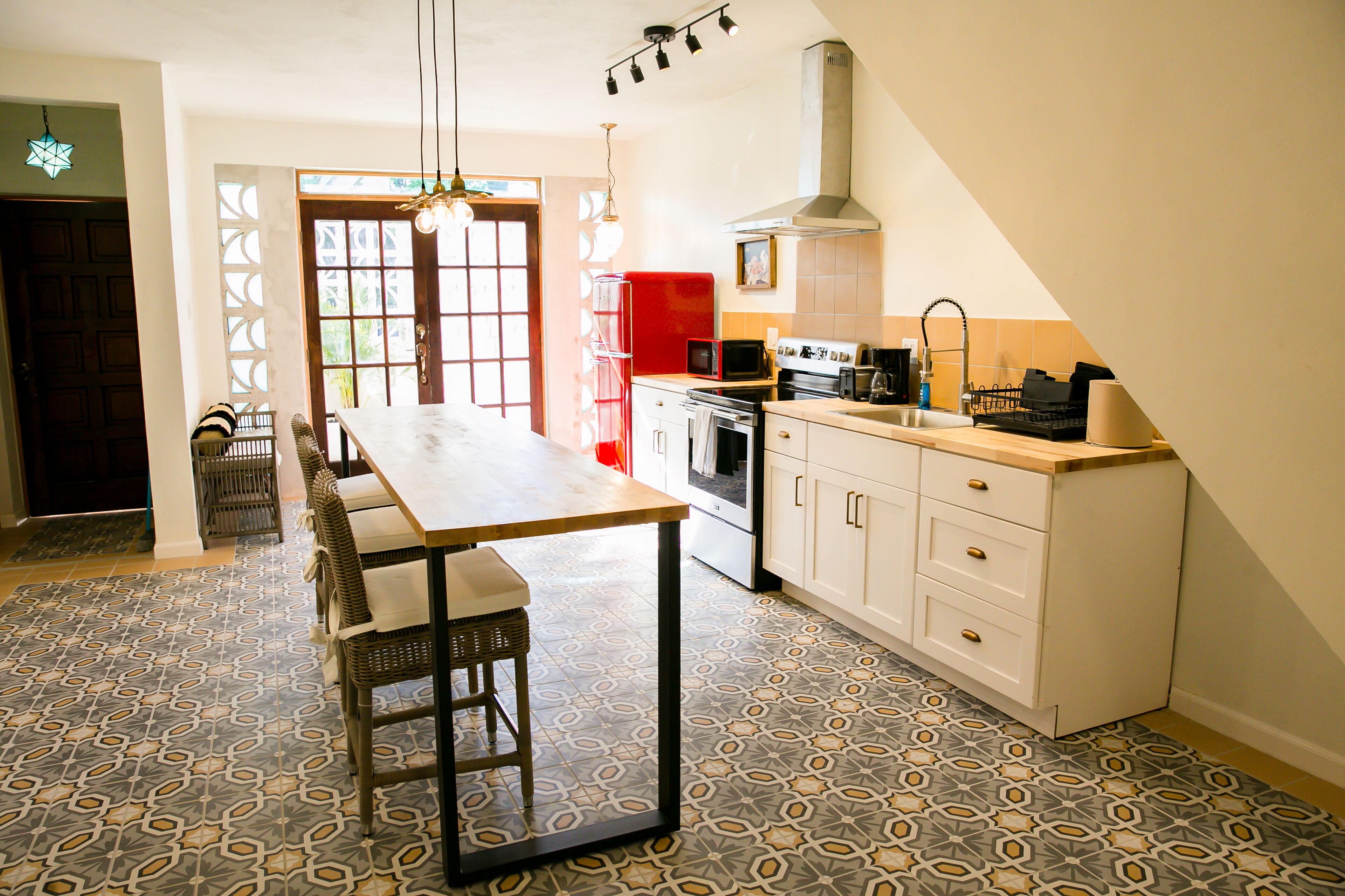 Una cocina con una isla central, armarios blancos, un electrodoméstico rojo y suelo estampado.