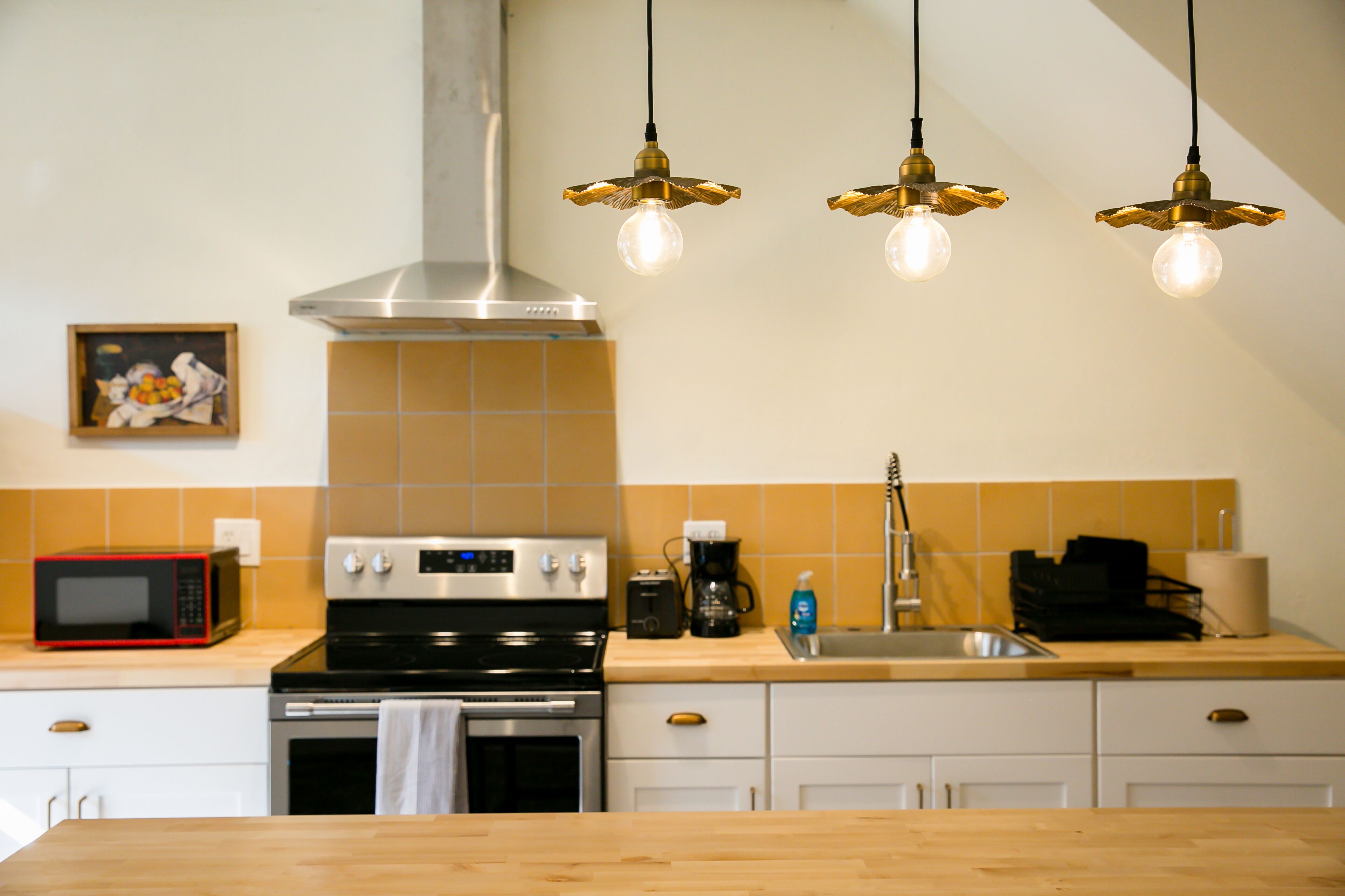 A kitchen with a stove, microwave, and a hanging light fixture.