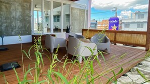 Un área de estar al aire libre con techo, terraza de madera, sillas modernas y vista panorámica de la ciudad.