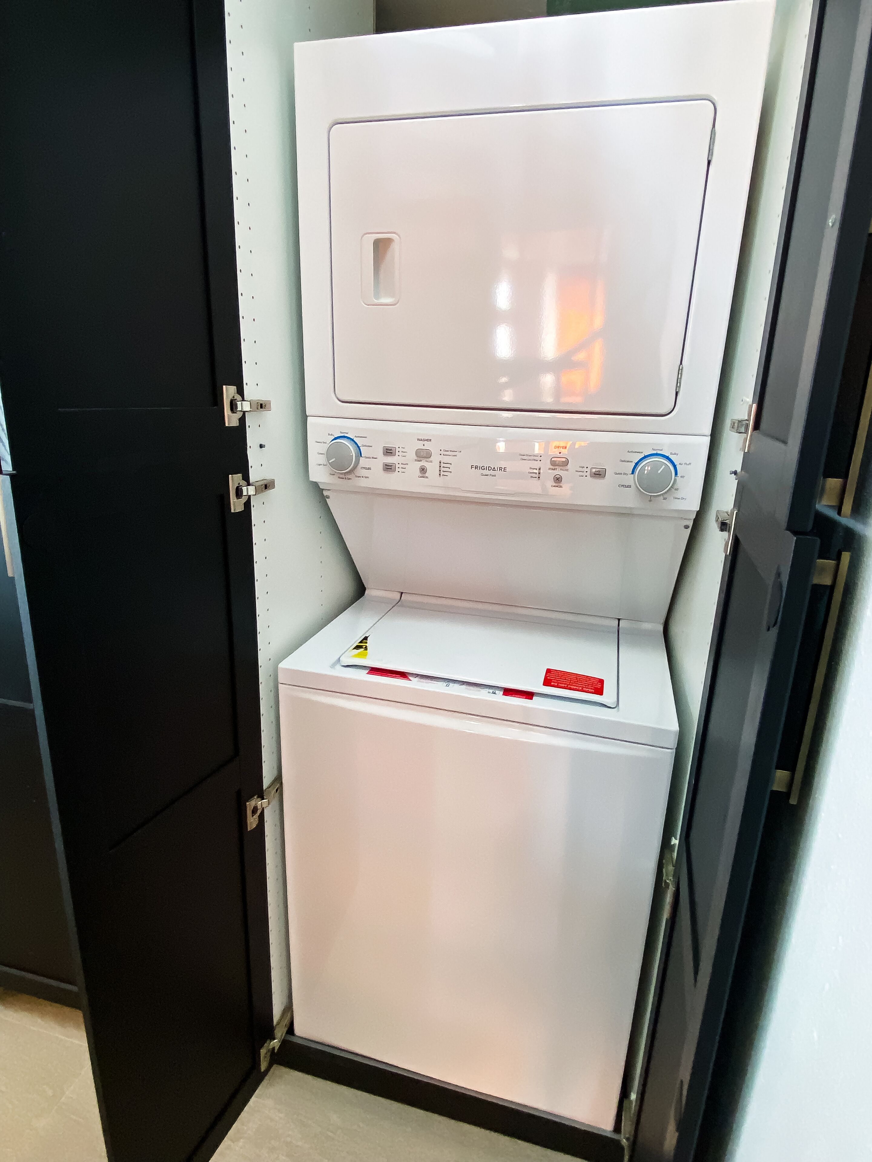 A compact, white laundry machine with a control panel, located in a room with a black door.
