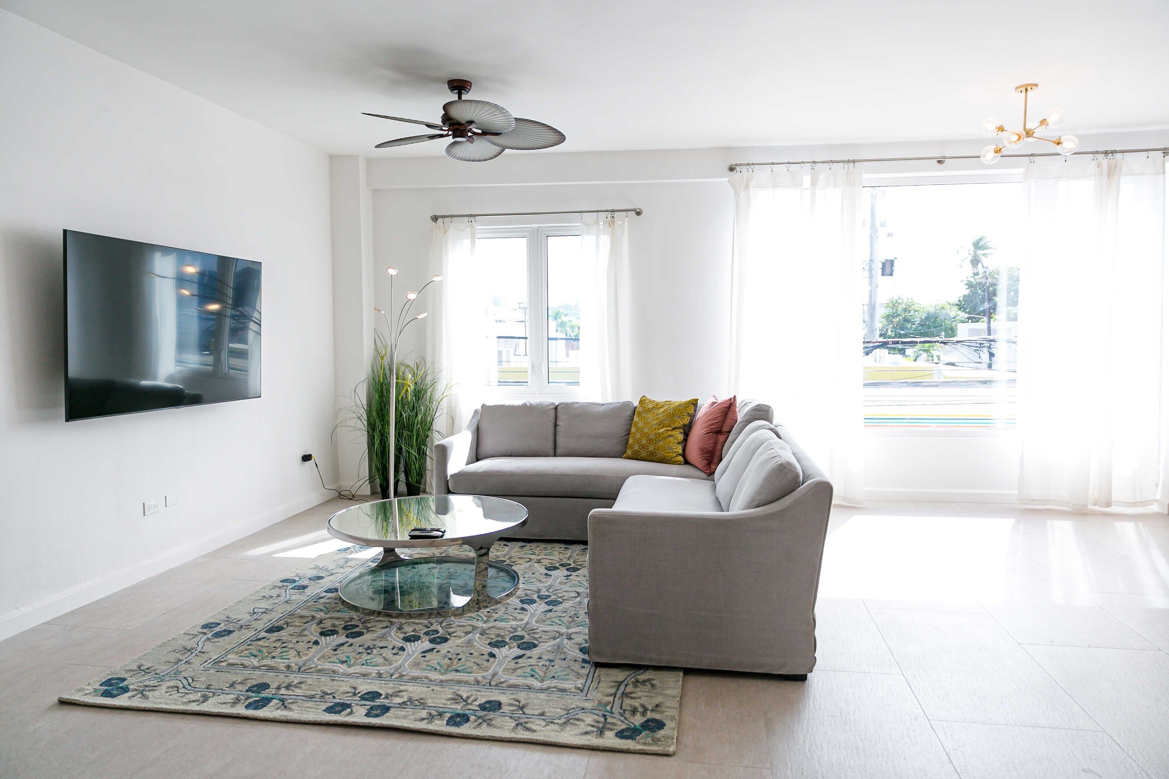 A modern living room with a sofa, a coffee table, a TV mounted on the wall, and a ceiling fan.