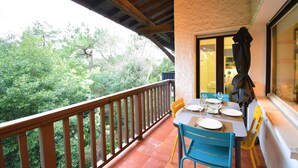 A balcony with a wooden railing, a table set for dining, and a view of greenery.