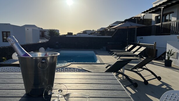 A poolside area with a metal bucket containing a bottle and glasses, lounge chairs, and a view of a pool and buildings in the background. - Luxery spacious 5 bedroom villa, private pool, jacuzzi, pooltable, aircon. bbq

 (Playa Blanca)