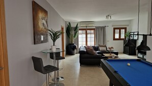 A living room with a pool table, a sofa, a dining table with chairs, and a large plant. - Luxery spacious 5 bedroom villa, private pool, jacuzzi, pooltable, aircon. bbq

 (Playa Blanca)