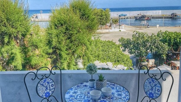 Un balcón con vista al mar, una mesita con una planta en maceta y un mantel de azulejos.