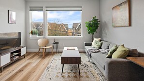 A modern living room with a sofa, coffee table, TV stand, and large windows offering a view of buildings.