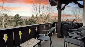 Une terrasse extérieure couverte, dotée d’une table et de chaises, qui offre une vue imprenable sur un paysage pittoresque, avec des arbres et un coucher de soleil.