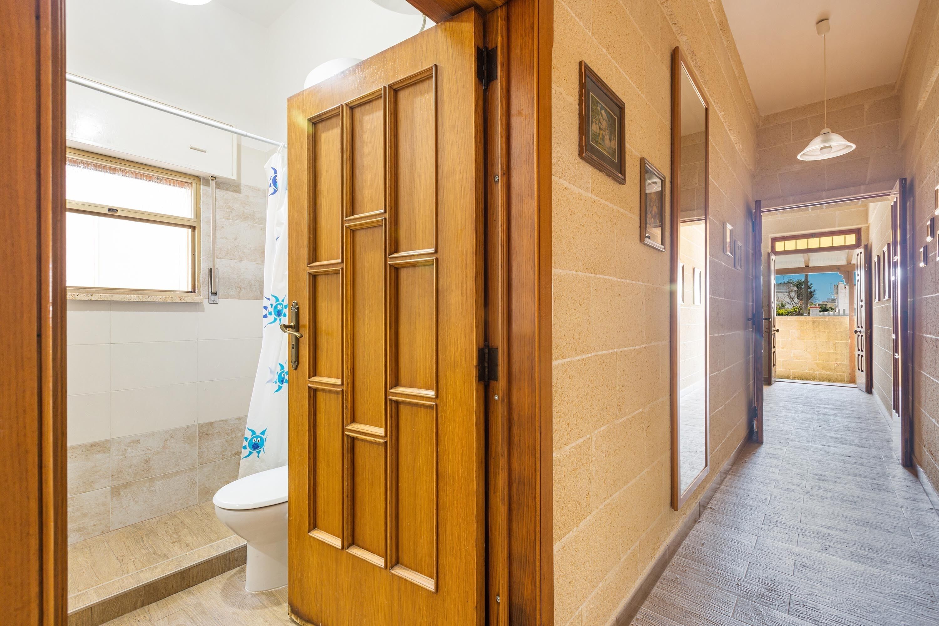 Un pasillo con puerta de madera, zona de ducha y suelo de baldosas.