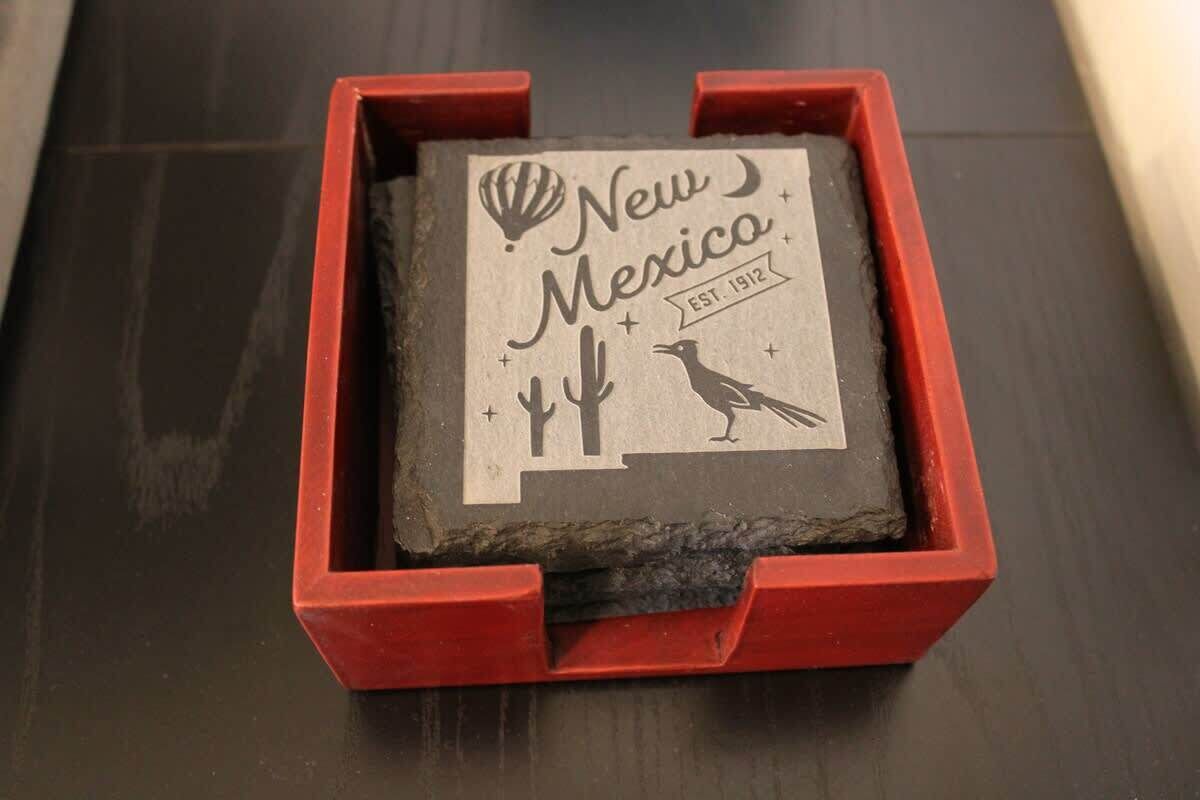 A red wooden box containing a black and white stamp with 'New Mexico' and 'EST. 1912' along with a cactus and bird illustration.