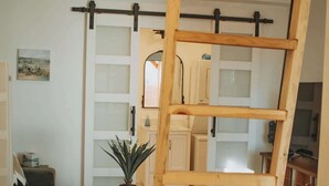 A loft-style room with a wooden ladder, a patterned rug, and a potted plant.
