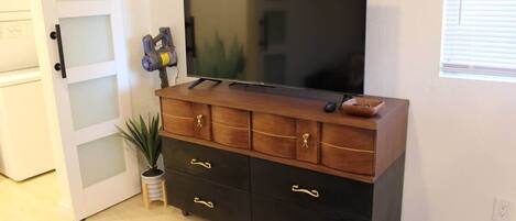 A room with a wooden cabinet, a flat-screen TV, a potted plant, and a door with frosted glass panels.