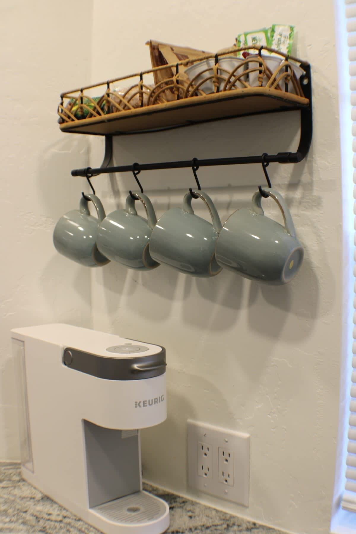Eine Küche mit einer Keurig-Kaffeemaschine und vier Tassen, die an einem Haken/Gestell hängen.