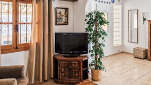A living room with a television on a wooden stand, a potted plant, a wooden cabinet, and a large mirror on the wall. - 2 bedroom amazing home in Orihuela (Orihuela)