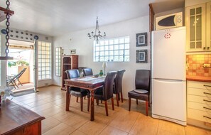 A dining area with a wooden table and chairs, a chandelier, and a kitchen with a white refrigerator and tiled backsplash.