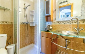 A bathroom with a glass sink, a shower, and a toilet.