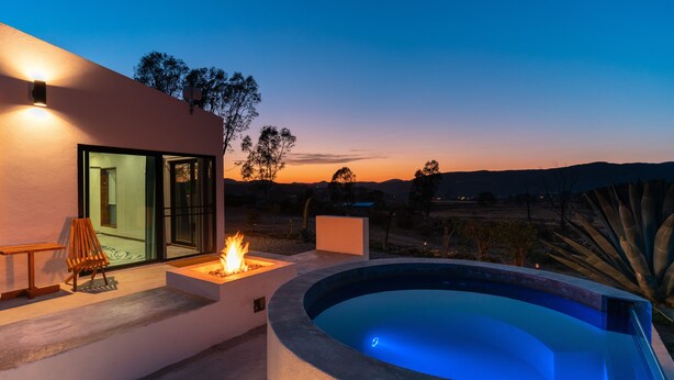 A modern outdoor pool area with a fire feature, seating, and a view of the landscape.