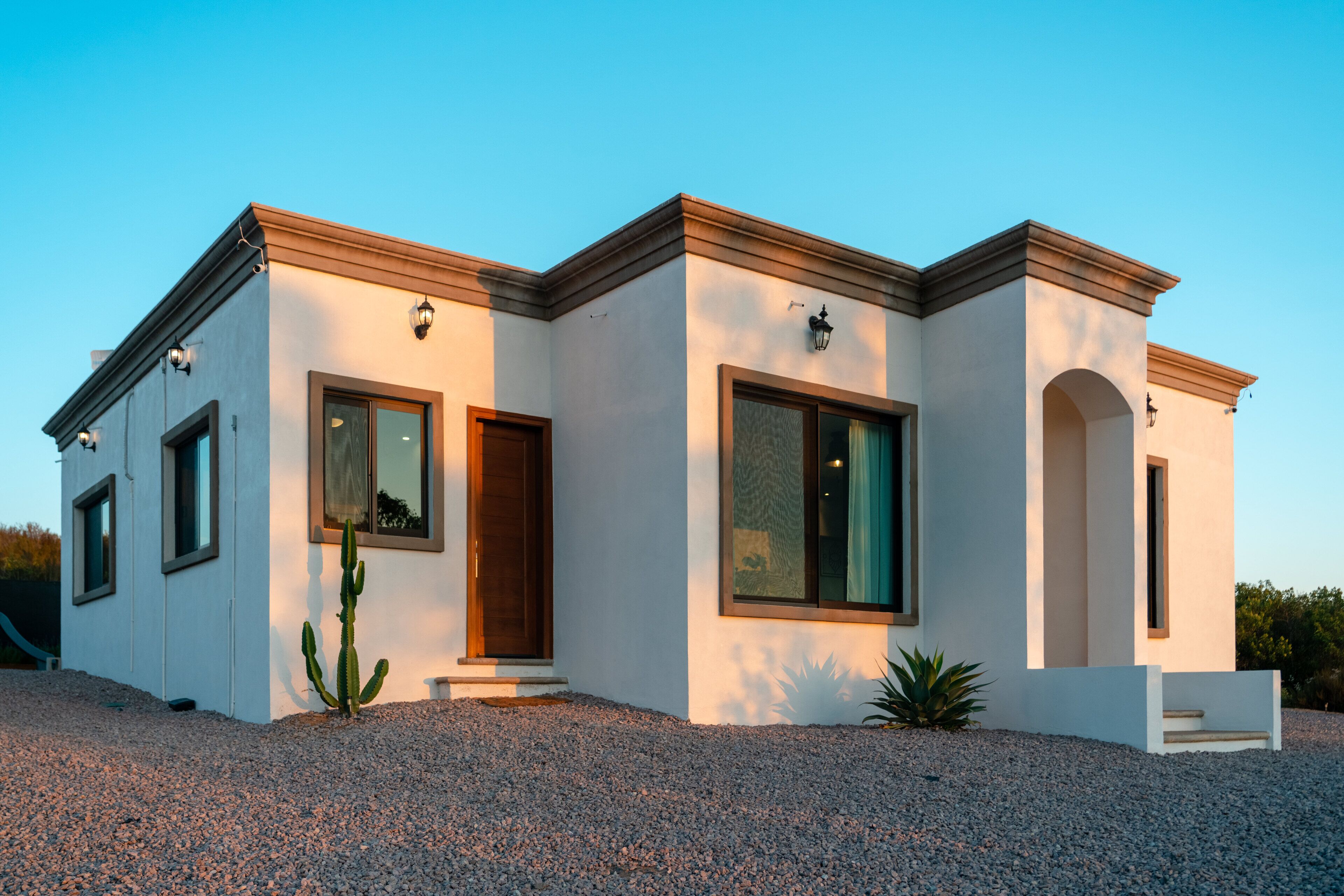 A modern two-story house with a white exterior, large windows, and a gravel driveway.