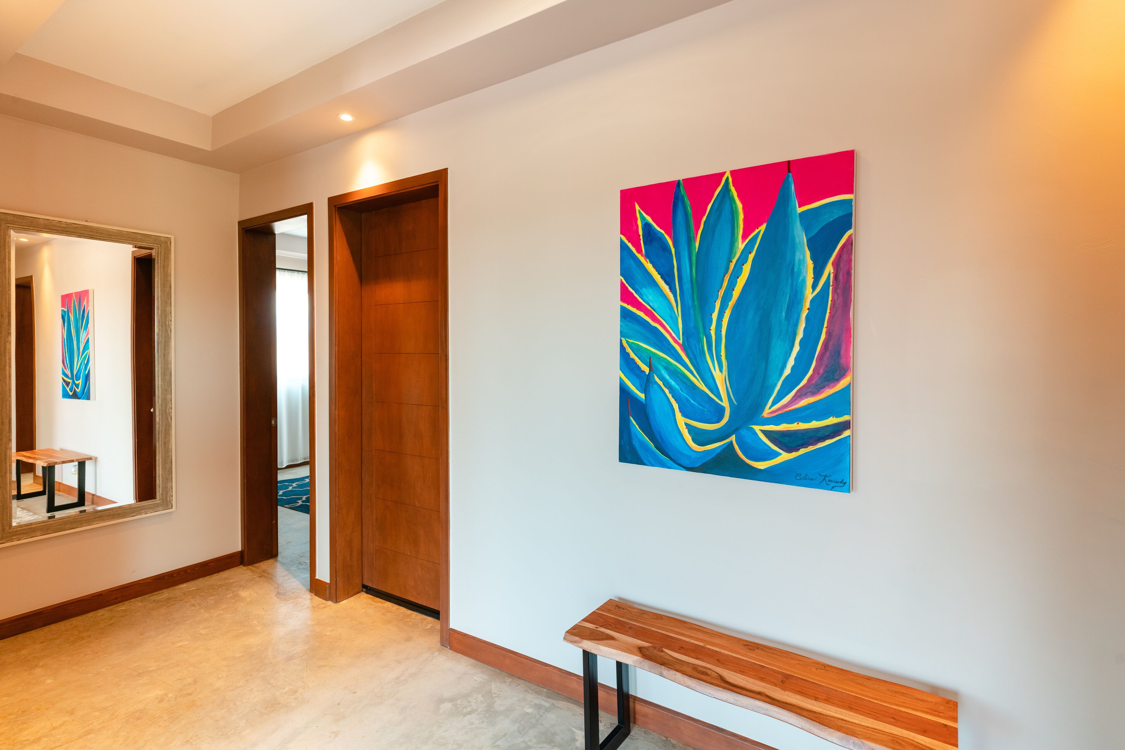 A hallway with a wooden bench, a large abstract painting, and a mirror reflecting part of the room.